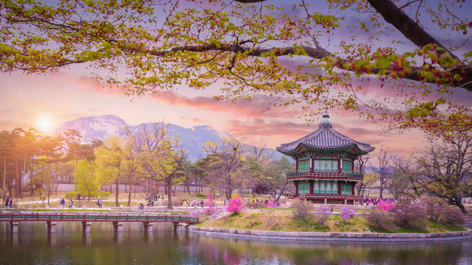 Đình Hyangwonjeong trên đảo nhỏ giữa hồ trong cung Gyeongbokgung, cây hoa mùa xuân và núi xa lúc hoàng hôn.