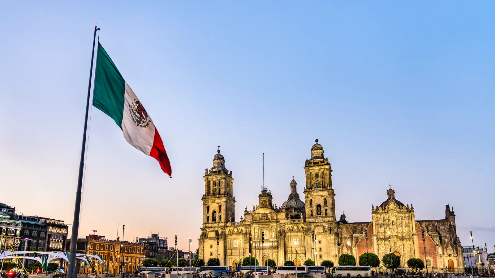 The Mexican flag flying beside the Metropolitan Cathedral in Mexico City at dusk.