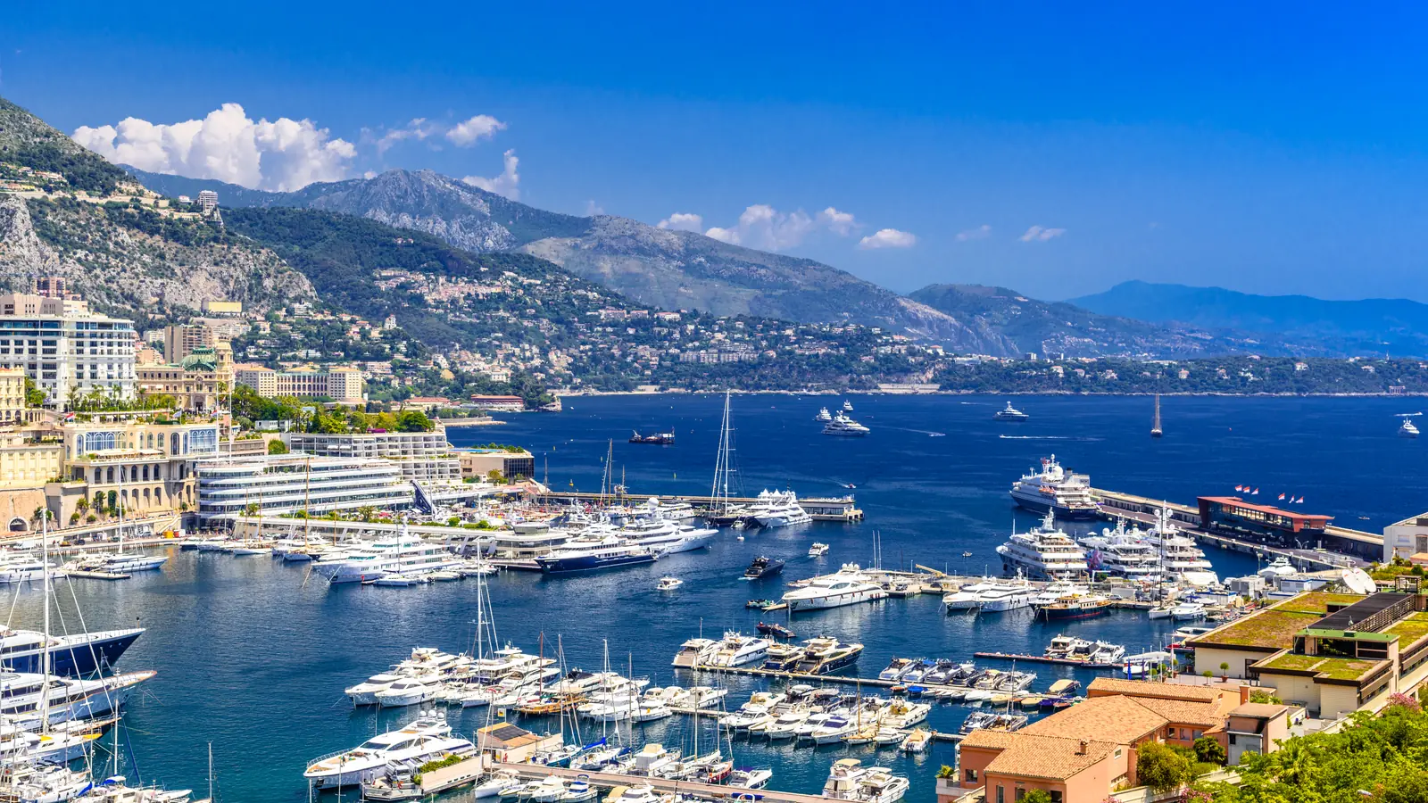 Du thuyền neo kín bến cảng Monaco, nhà cửa trải dọc bờ biển dưới chân núi.
