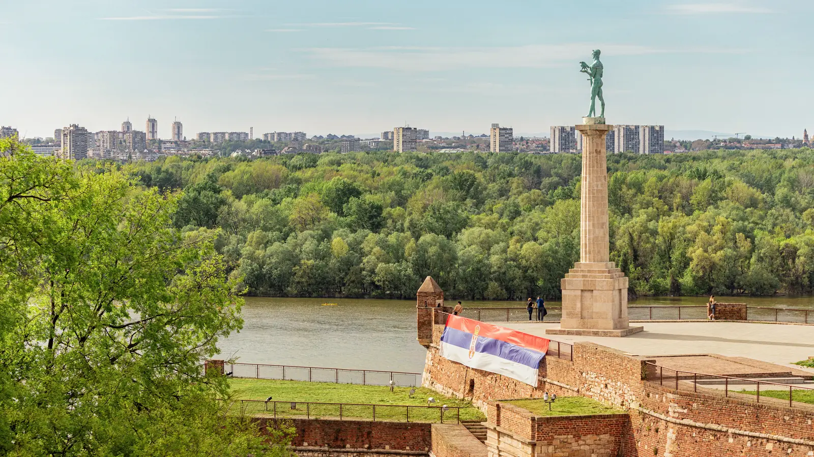 The Victor monument on its column at Kalemegdan fortress in Belgrade, a Serbian flag on the ramparts and tower blocks across the river.