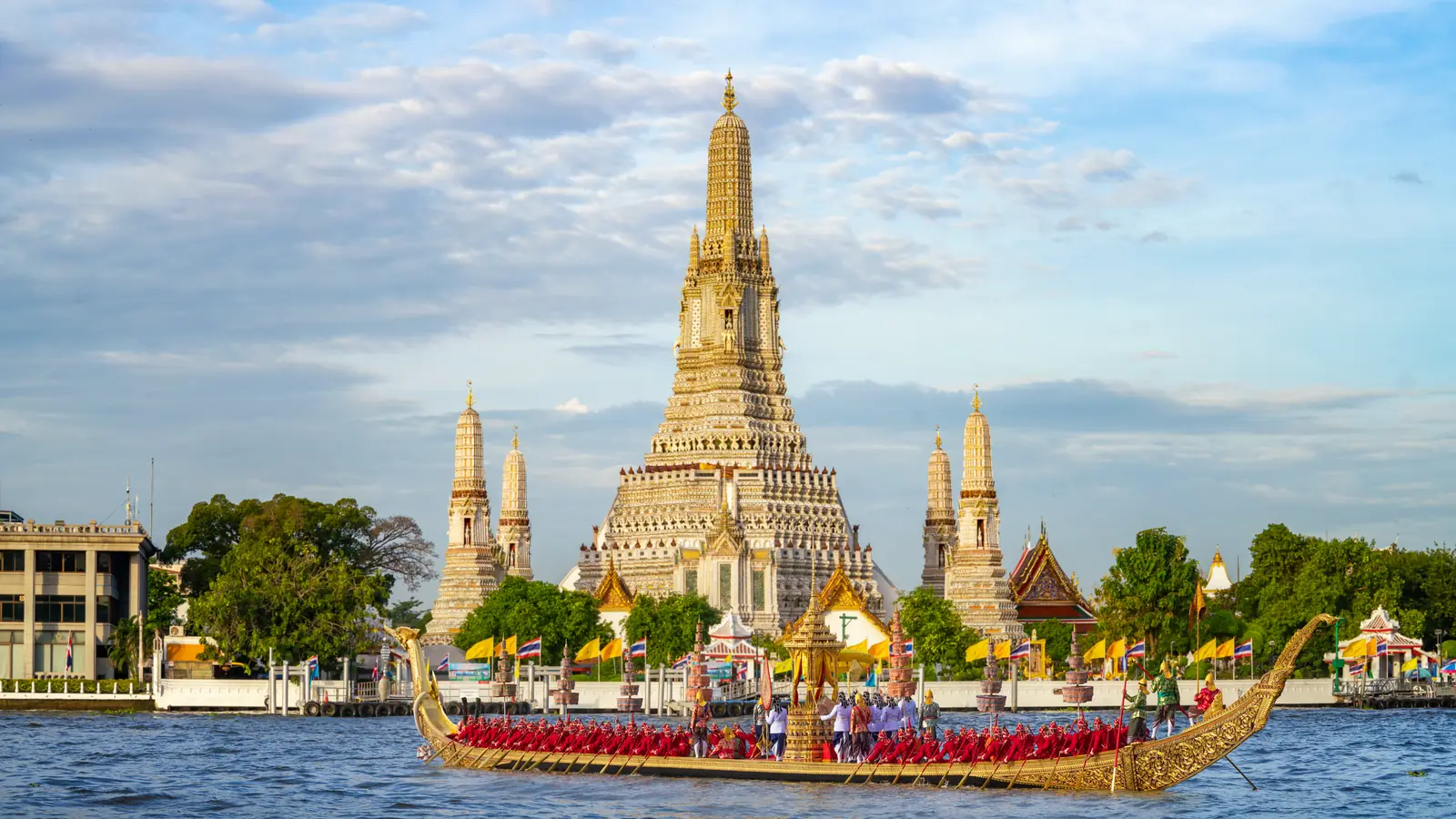 Chùa Wat Arun bên sông Chao Phraya ở Bangkok, một thuyền rồng hoàng gia chở đầy người chèo đi ngang phía trước.