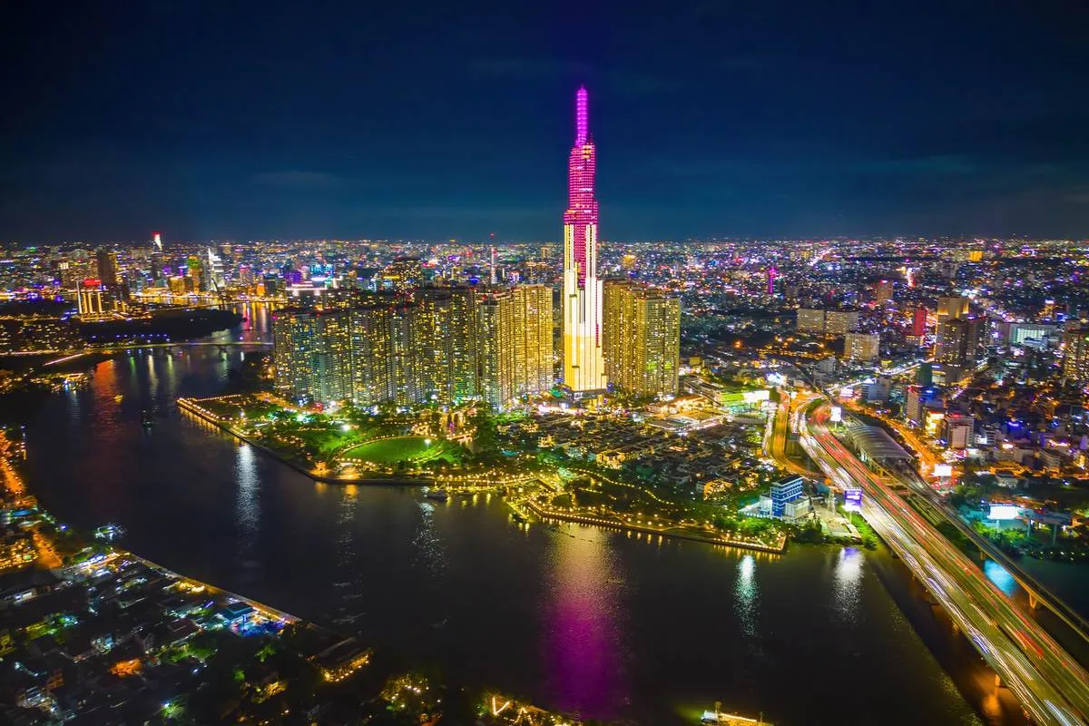 Toà Landmark 81 thắp sáng về đêm bên sông Sài Gòn, có khu trung tâm và cầu Ba Son trong khung hình.