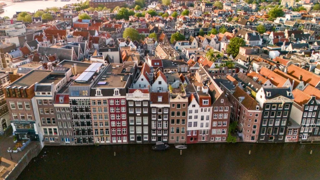 Aerial view of narrow brick canal houses along the water and dense red rooftops in Amsterdam