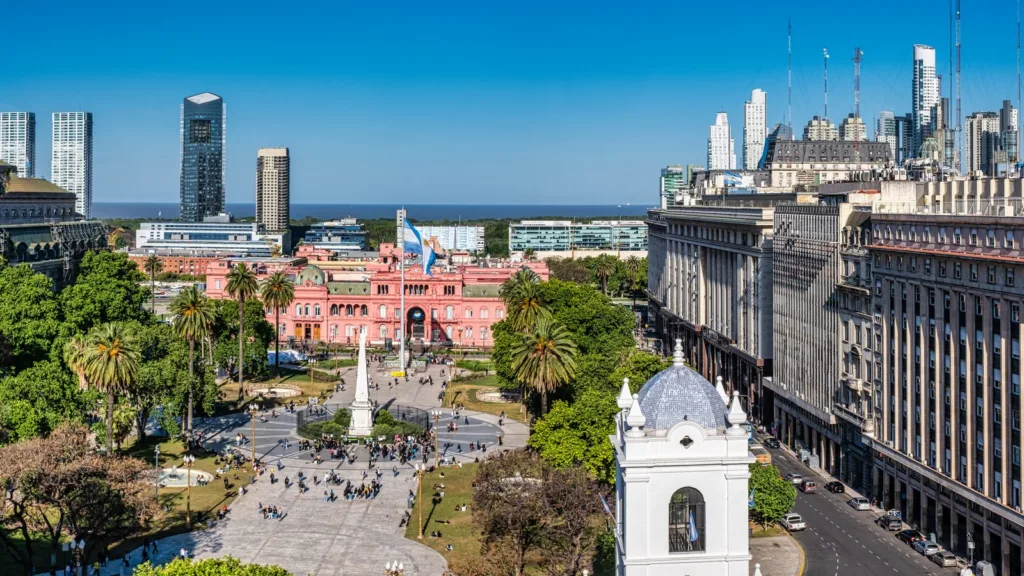 Quảng trường Mayo ở Buenos Aires nhìn từ trên cao, với Casa Rosada màu hồng, một đài tưởng niệm hình tháp nhọn, hàng cọ, người qua lại trên quảng trường và các toà văn phòng phía sau.