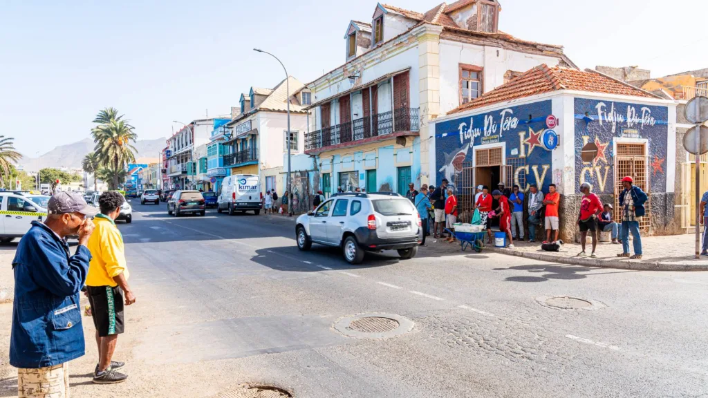 People gathered outside a shop with a painted mural on a street of colonial houses in Mindelo, Cabo Verde.