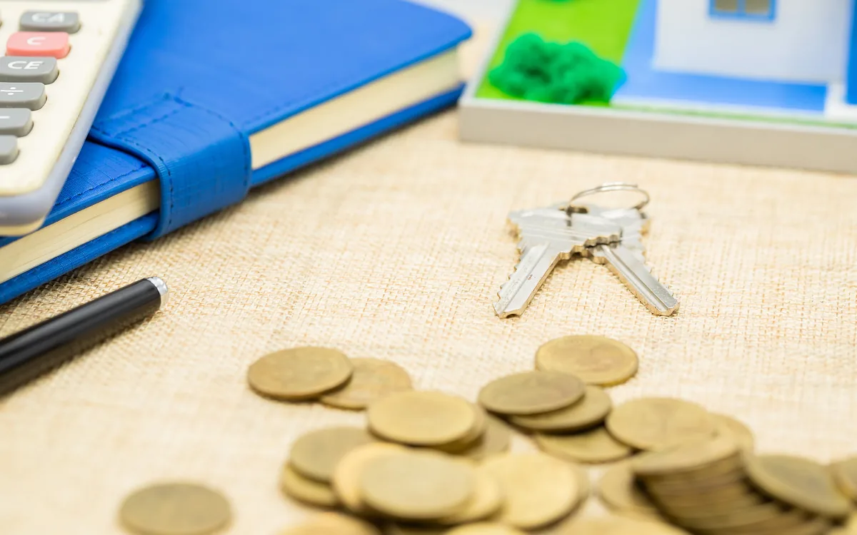 A notebook, a pocket calculator, a bunch of keys and a pile of gold coins on a table.