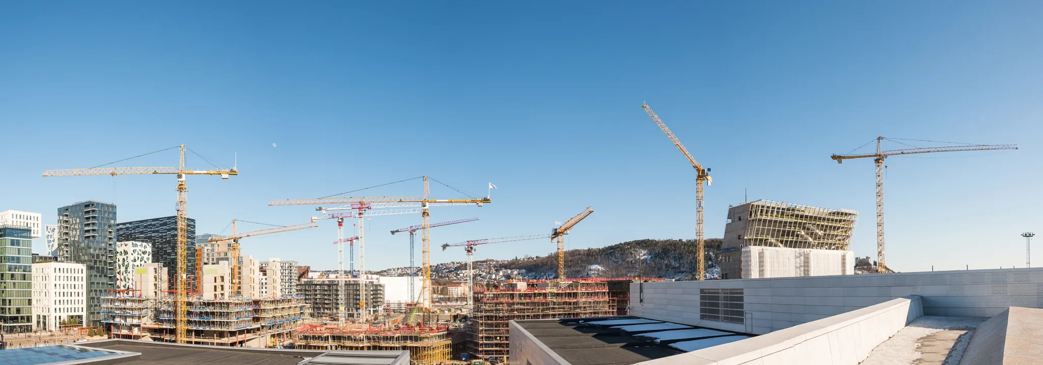 Dozens of tower cranes over a new urban district under construction, new blocks rising towards the foot of the hills.