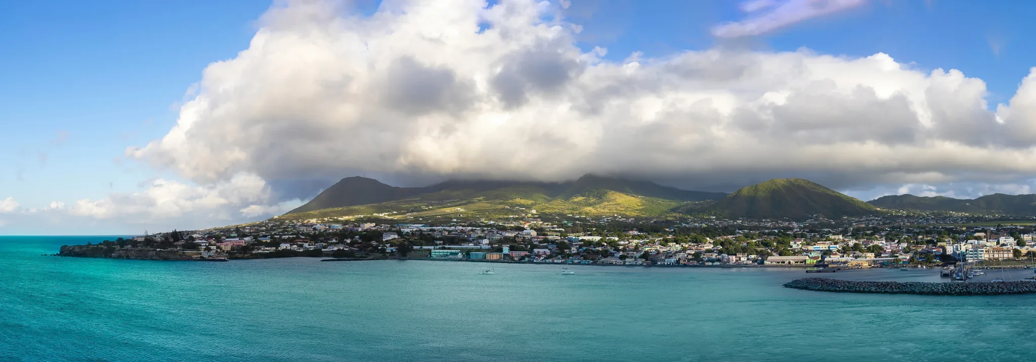 The town of Basseterre along the shore of Saint Kitts, a forested mountain behind and turquoise water in front.