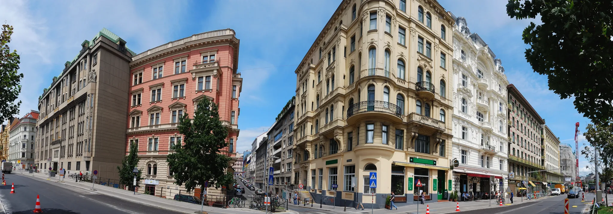 A Vienna street corner with two rows of multi-storey apartment buildings, ornate facades and shops on the ground floor.