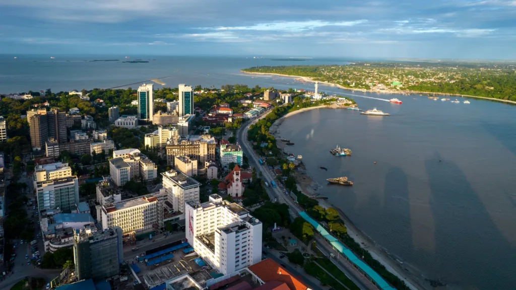 Central Dar es Salaam from above, with office towers, the harbour entrance, ferries and the green Kigamboni shore across the water