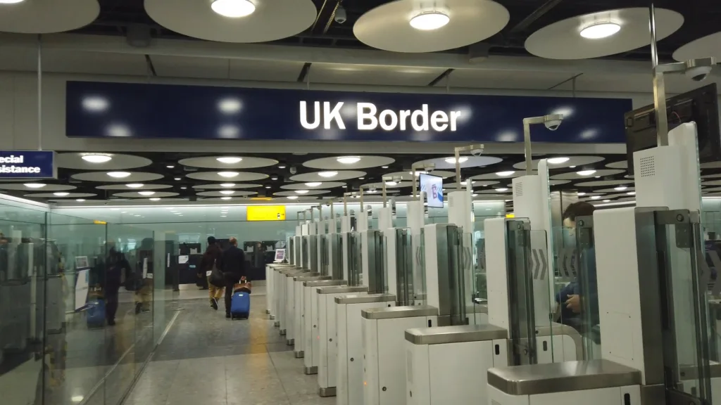 Cổng kiểm soát hộ chiếu tự động dưới tấm biển UK Border ở sân bay Heathrow, hành khách đi lại phía sau.