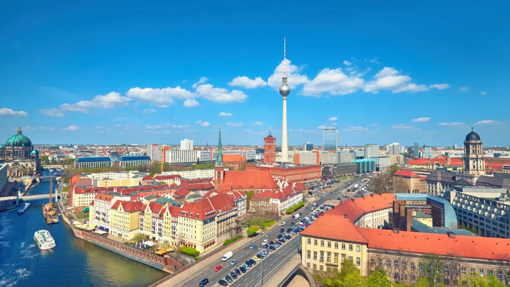 Aerial view of central Berlin on a sunny day, with the River Spree, red-roofed buildings, a busy road and the television tower on the skyline