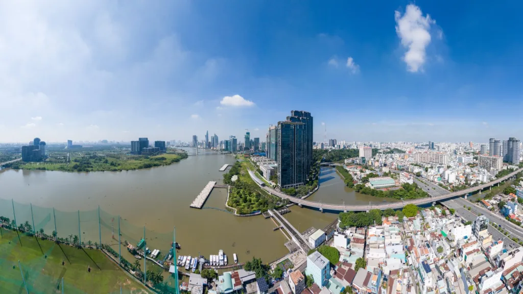 Wide aerial view of the Saigon River bending past high-rise towers, a bridge and dense low-rise housing in Ho Chi Minh City, Vietnam