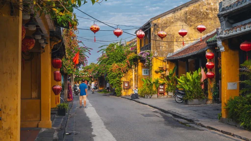 Du khách đi bộ trên một con phố cổ Hội An với những ngôi nhà tường vàng, đèn lồng đỏ và giàn hoa giấy