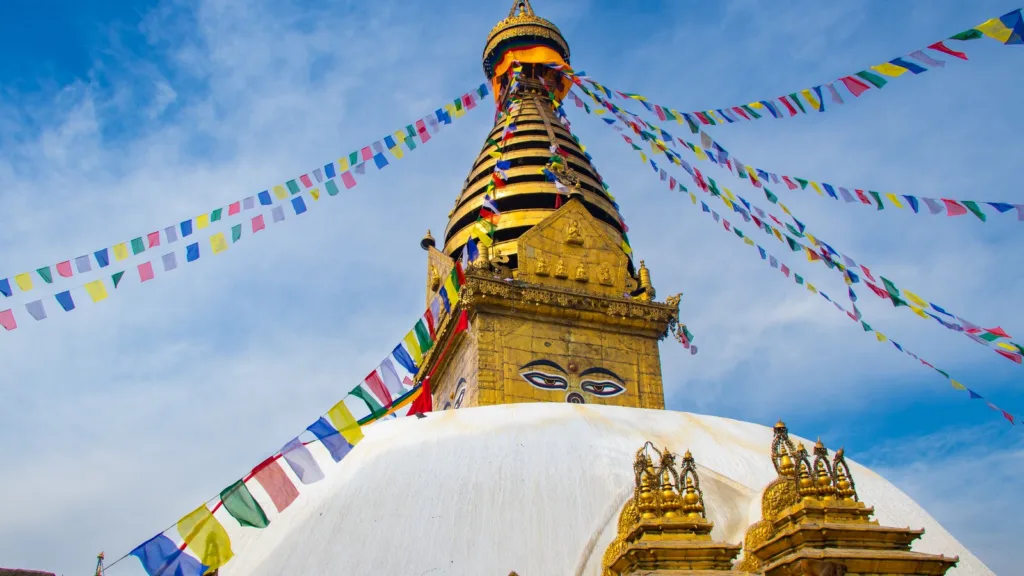 Swayambhunath stupa in Kathmandu, with its gilded spire, painted Buddha eyes and strings of coloured prayer flags against a blue sky