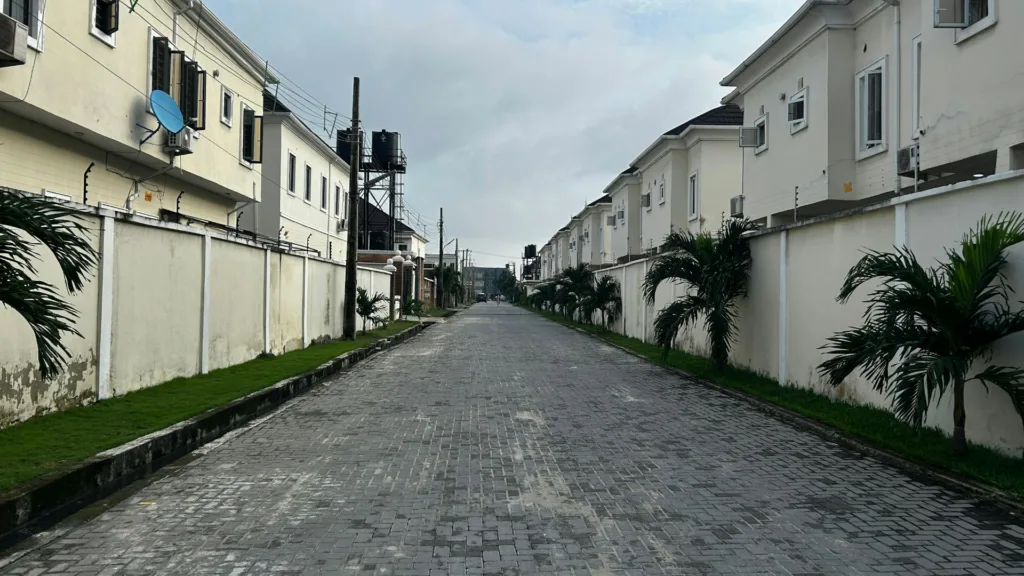 Con phố lát nhựa trong một khu dân cư có cổng ở Lagos, Nigeria, hai bên là nhà hai tầng.