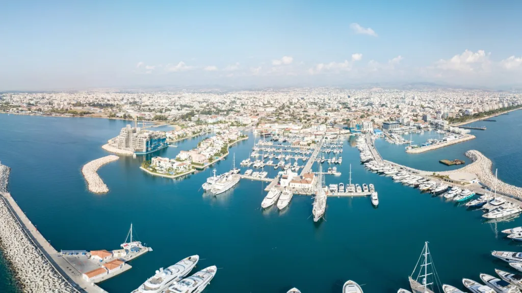 Limassol Marina in Cyprus seen from above, with yachts moored inside stone breakwaters, a small island of villas and the city stretching behind