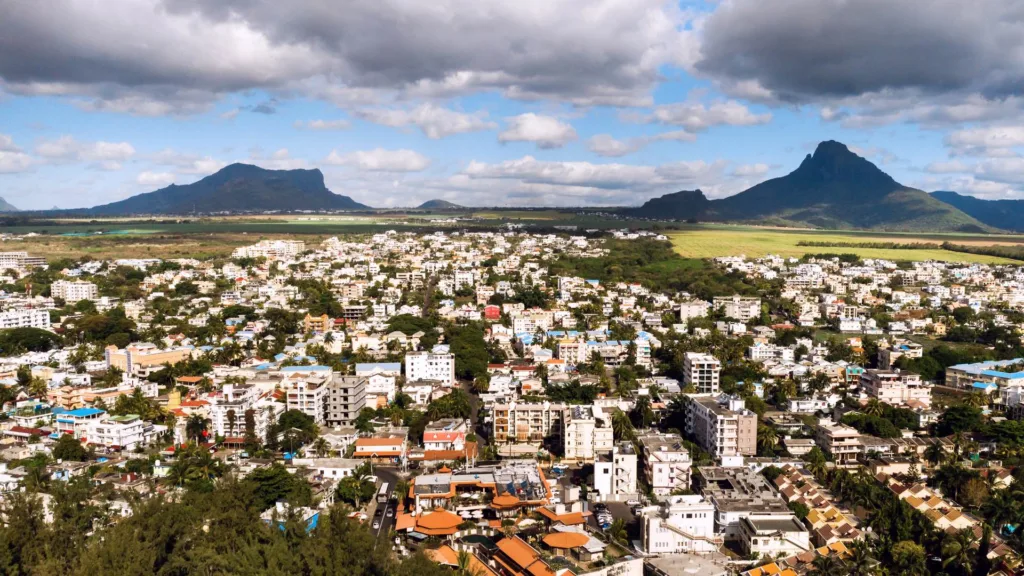 Một thị trấn dân cư dày đặc nhà ở và khối căn hộ thấp tầng trên đảo Mauritius, phía sau là ruộng mía và hai dãy núi.