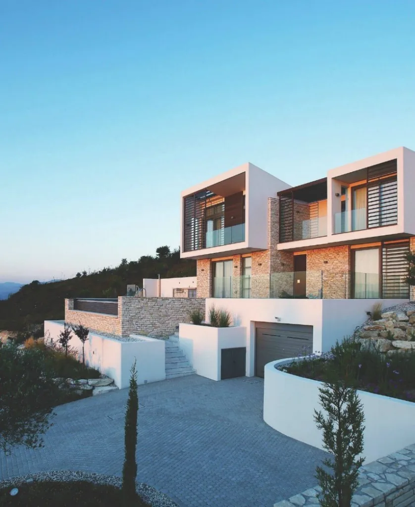 Flat-roofed buildings stepped down a hillside, white walls and dark timber, with cypress trees between them.