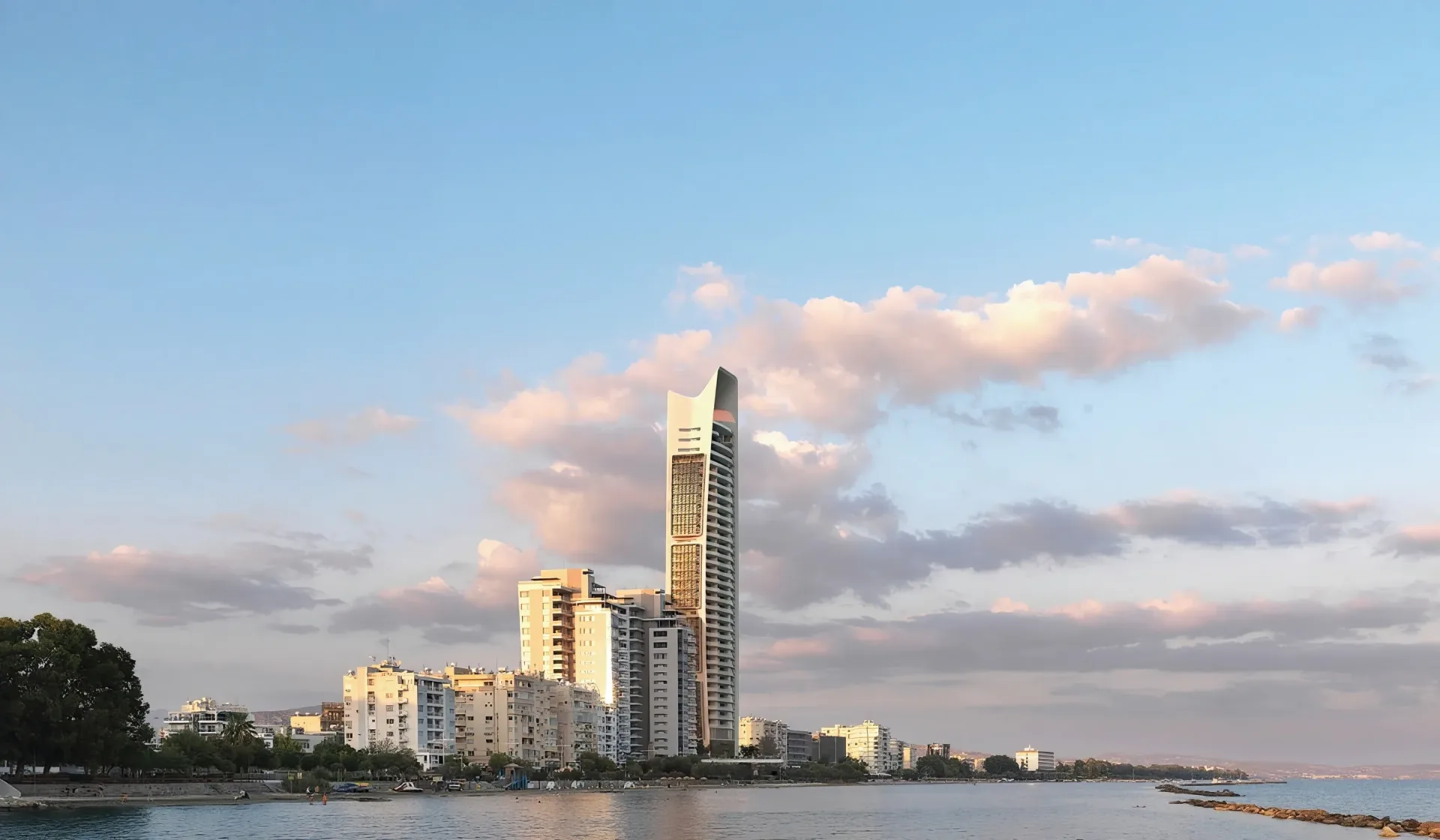 A tall glass apartment tower on the Limassol seafront, seen from the water in the afternoon.