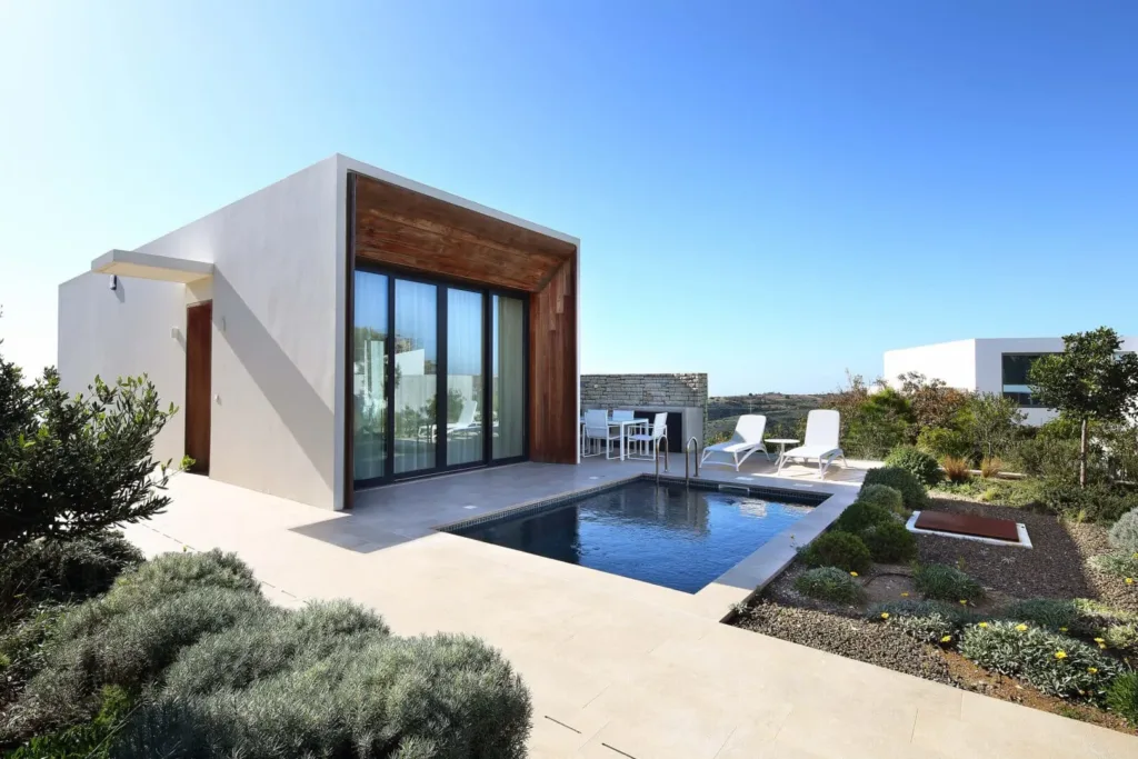 White villa with timber-framed glazing beside a plunge pool and drought-tolerant garden