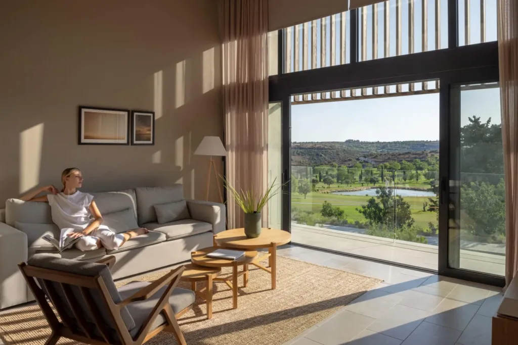 Double-height living room opening to a balcony overlooking the golf course, a woman seated on the sofa