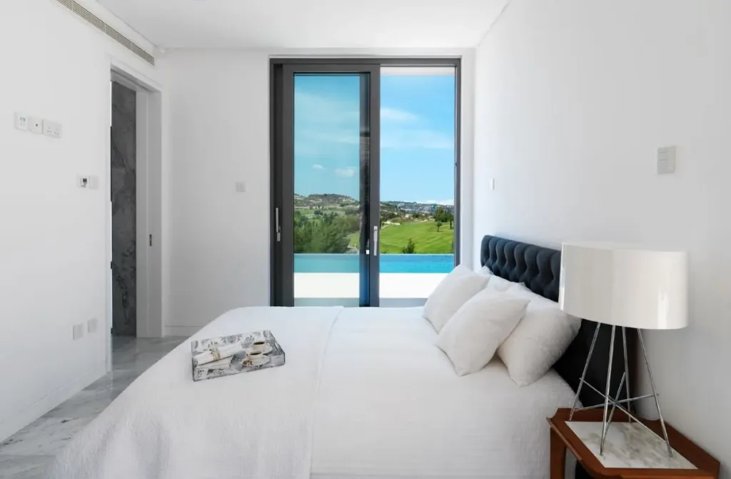 White bedroom with a glass door looking out to the pool and golf course