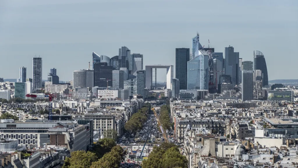 Các toà tháp khu La Défense và Grande Arche nhìn qua những mái nhà Paris dọc một đại lộ có hàng cây.