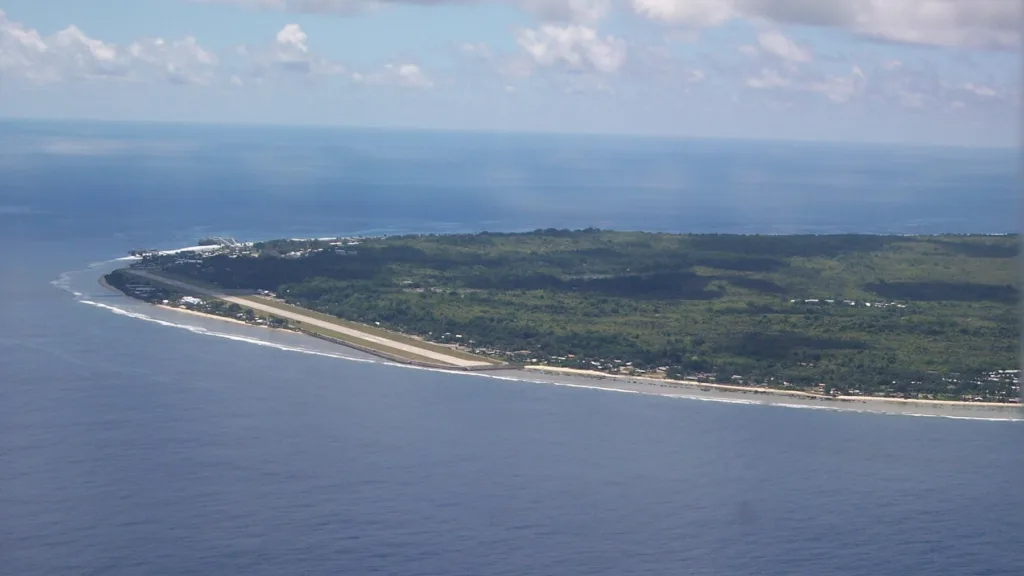 Đảo Nauru nhìn từ máy bay: Đường băng chạy dọc bờ biển, rìa rạn san hô bao quanh đảo, phần trong đảo phủ cây xanh