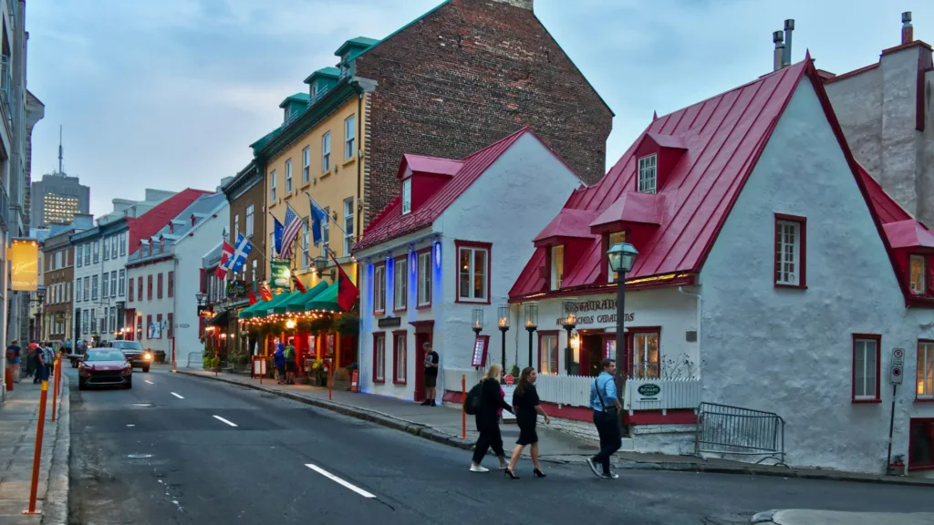 Three people cross Rue Saint-Louis in Old Quebec at dusk, past red-roofed stone houses