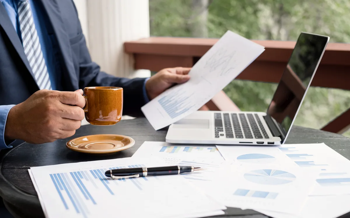 A businessman holding a cup of coffee, his hand resting on a desk.