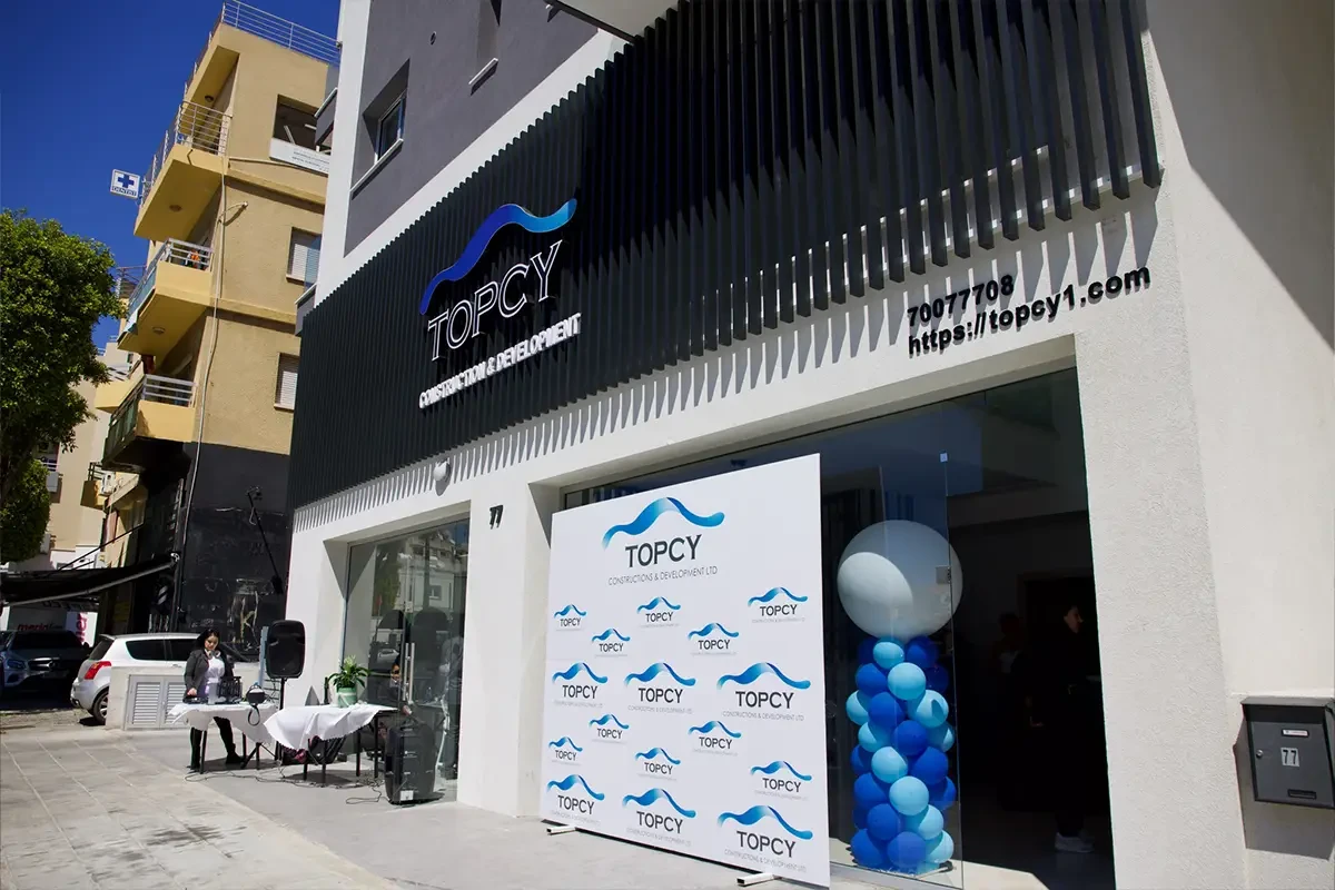 Mặt tiền văn phòng TOPCY ốp lam đen, biển logo sóng xanh và chữ TOPCY Construction & Development, phía dưới là phông nền logo và cột bóng bay xanh trắng
