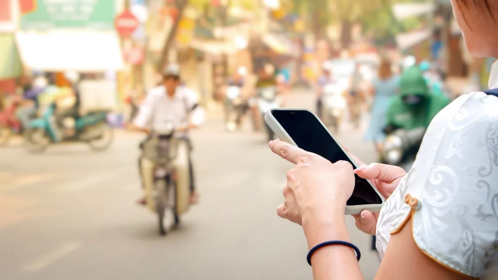 A woman holds a smartphone on a street in Vietnam as motorcyclists ride behind her