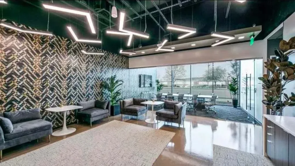 Phòng chờ văn phòng với sofa xám, tường ốp gạch xương cá màu tối và đèn trần dạng thanh, cửa kính nhìn ra ngoài
