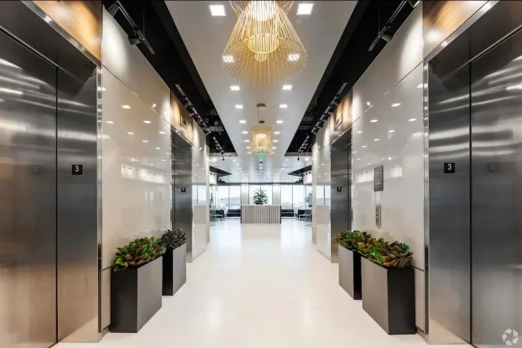 Sảnh thang máy ốp kim loại với đèn chùm và chậu cây hai bên