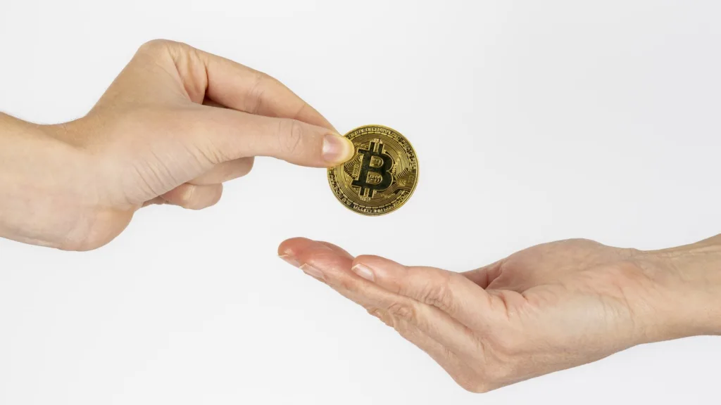 Một bàn tay trao đồng bitcoin màu vàng vào lòng bàn tay mở của người khác