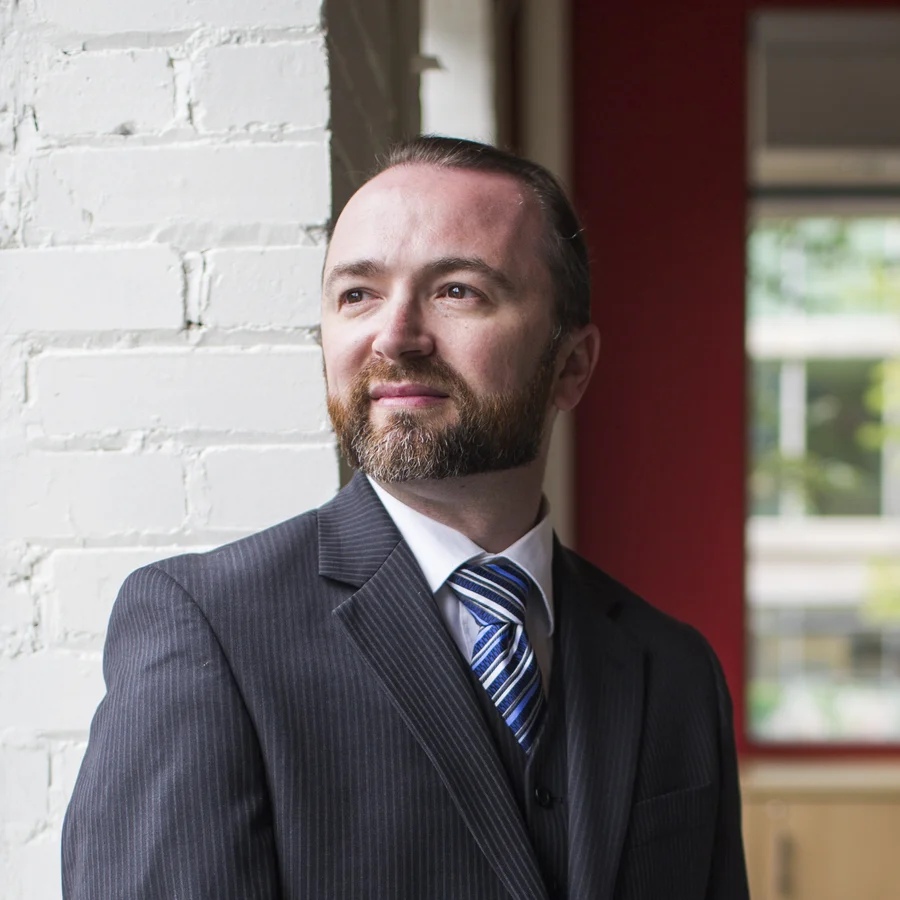 Portrait of Slava Apel in a pinstripe suit, standing by a window