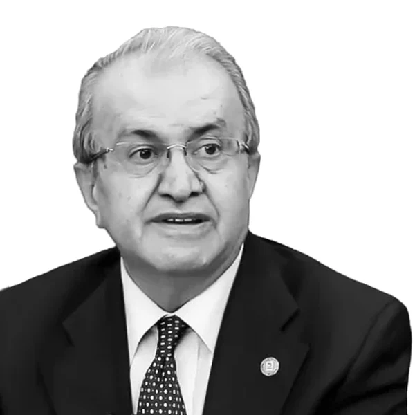 Black-and-white portrait of Kemal Özmen, grey-haired and wearing glasses, a dark suit, white shirt and polka-dot tie, with a pin on his lapel