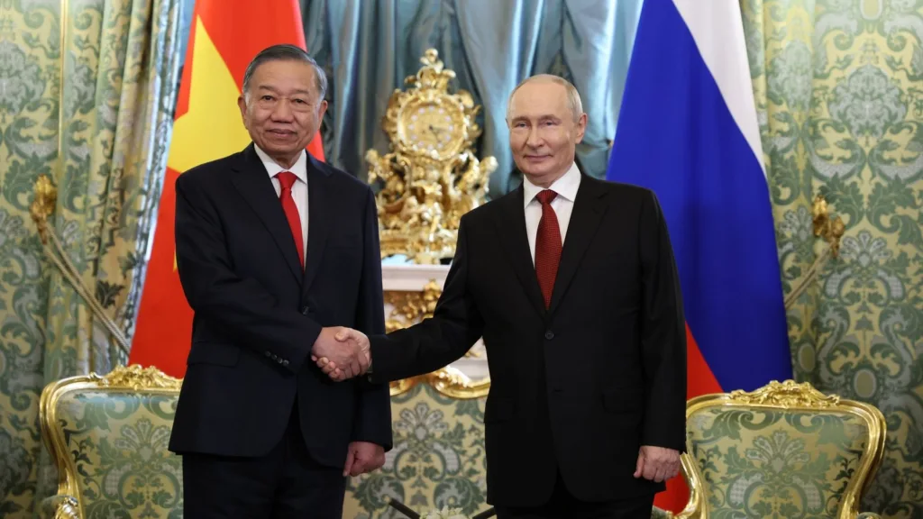 Russian President Vladimir Putin, right, and Vietnam's President To Lam, left, shake hands in front of the Russian and Vietnamese flags in a hall with green damask walls and a gilded clock