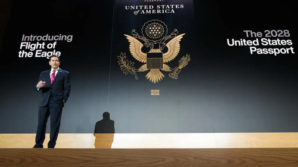 Ngoại trưởng Marco Rubio đứng trên sân khấu trước màn hình chiếu bìa hộ chiếu Hoa Kỳ mới với quốc huy chim đại bàng vàng và dòng chữ The 2028 United States Passport