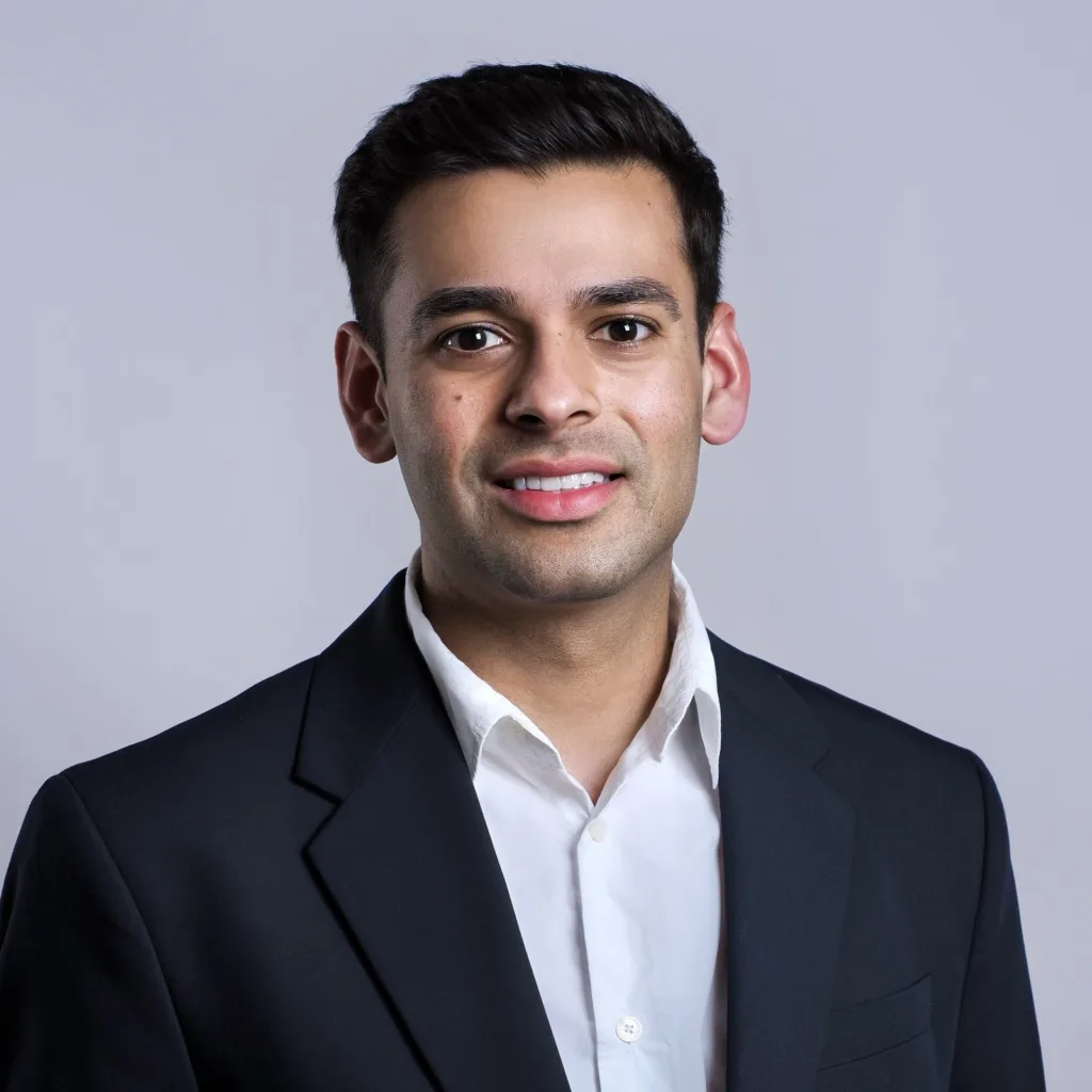 Portrait of Akhil Sahu in a dark blazer and white shirt against a light grey background